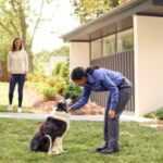 A pest control technician leaning down to pet a dog at a home they are servicing.