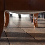 A close-up view of wooden furniture legs on a hardwood floor, with several cobwebs—suggesting a possible spider infestation—connecting the legs and dust on the wood.