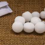 Several white camphor mothballs of varying sizes are spread on a brown burlap surface, with a partially opened white paper packet visible on the left side of the image, highlighting common uses and potential risks.